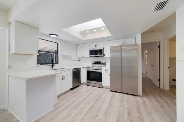 kitchen with a raised ceiling, sink, white cabinets, stainless steel appliances, and light wood-type flooring