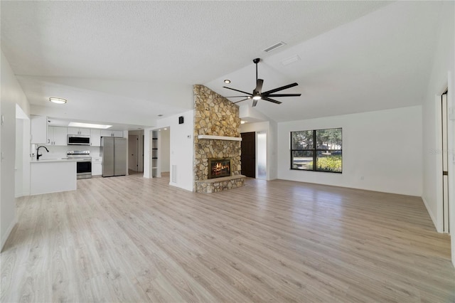 unfurnished living room featuring a stone fireplace, lofted ceiling, sink, ceiling fan, and light wood-type flooring