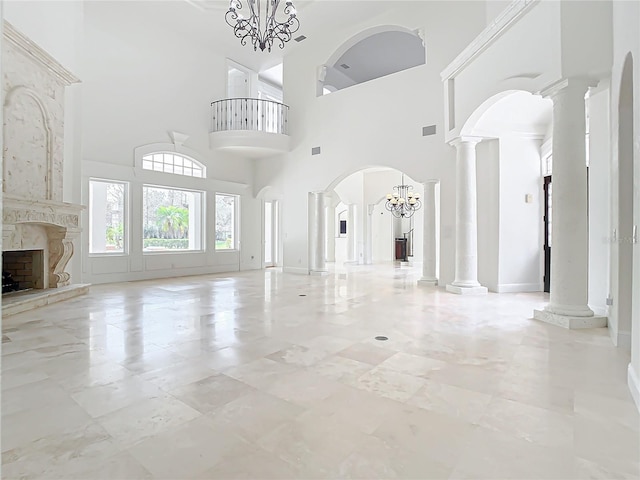 unfurnished living room featuring a high end fireplace, a chandelier, and ornate columns