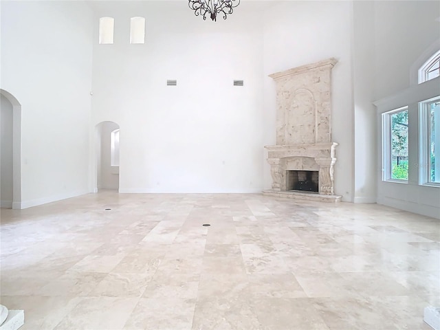 unfurnished living room featuring a fireplace, a chandelier, and a high ceiling