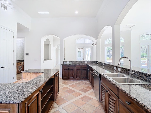 kitchen featuring sink, dark stone counters, a center island, stainless steel dishwasher, and dark brown cabinets