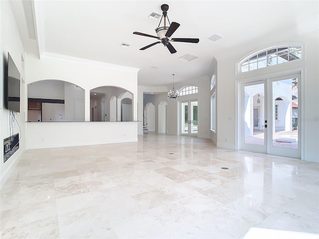 unfurnished living room with crown molding, ceiling fan with notable chandelier, french doors, and a high ceiling