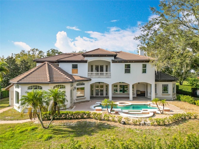 back of house featuring a balcony, a pool with hot tub, a patio, and a lawn