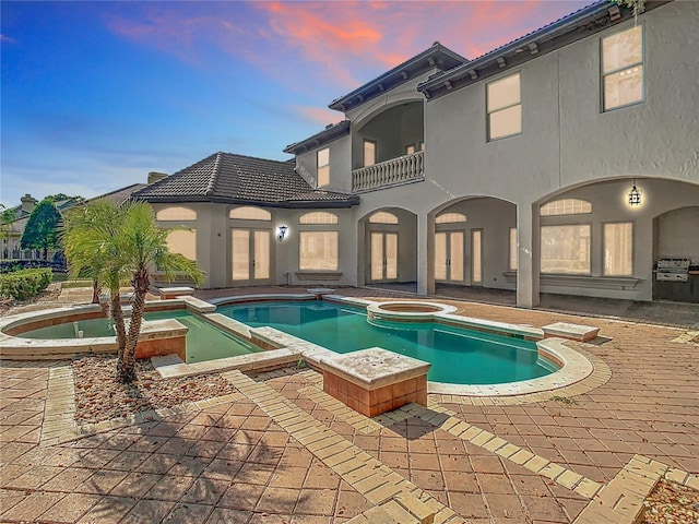 pool at dusk featuring an in ground hot tub and a patio