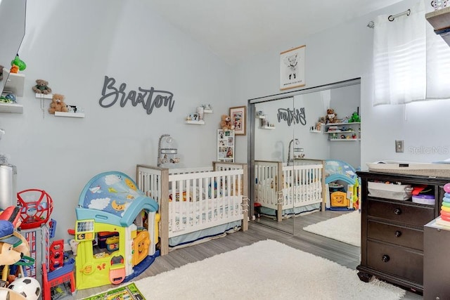 bedroom with lofted ceiling, a crib, wood-type flooring, and a closet