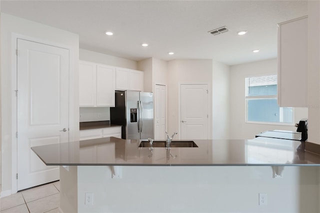 kitchen with a breakfast bar, stainless steel fridge with ice dispenser, white cabinets, range, and kitchen peninsula