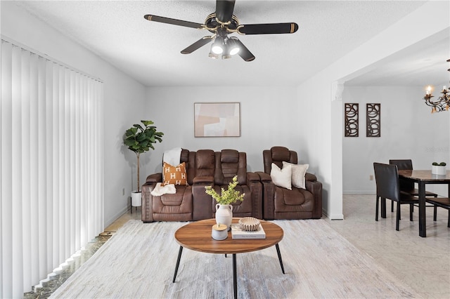 living room featuring ceiling fan with notable chandelier and a textured ceiling