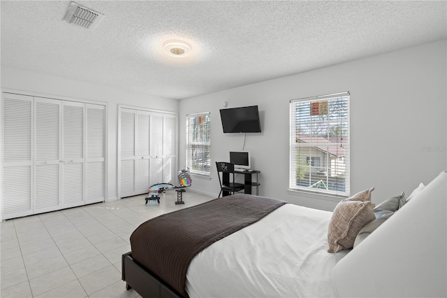 tiled bedroom featuring multiple closets, multiple windows, and a textured ceiling
