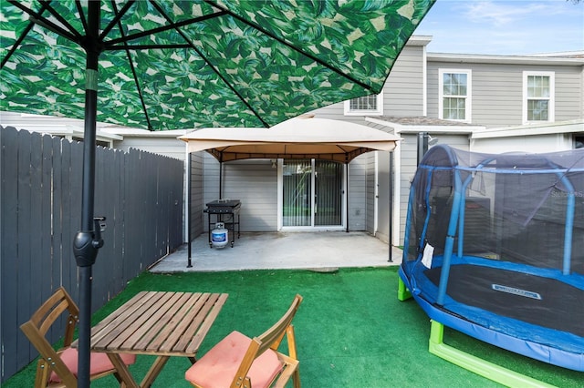 rear view of property featuring a gazebo, a patio area, a trampoline, and a lawn
