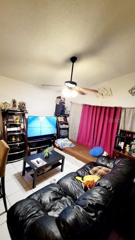 living room featuring ceiling fan, a textured ceiling, and tile patterned floors