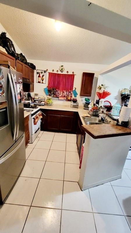 kitchen featuring a peninsula, light tile patterned floors, stainless steel fridge, and white gas stove