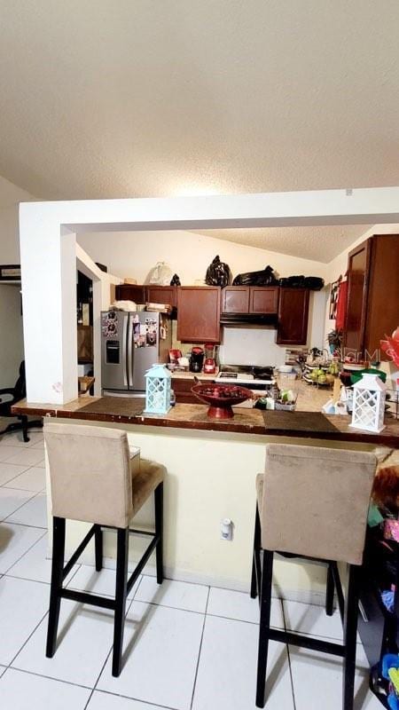 1417 Brookebridge Dr, Orlando, FL 32825 - kitchen featuring a breakfast bar area, dark countertops, light tile patterned flooring, a peninsula, and stainless steel fridge with ice dispenser
