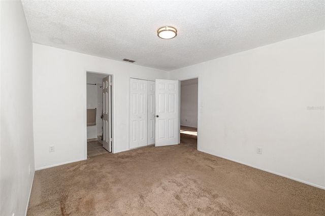 unfurnished bedroom featuring light colored carpet, ensuite bath, a closet, and a textured ceiling