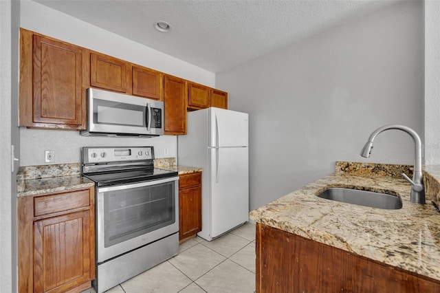 kitchen featuring sink, appliances with stainless steel finishes, light stone counters, a textured ceiling, and light tile patterned flooring