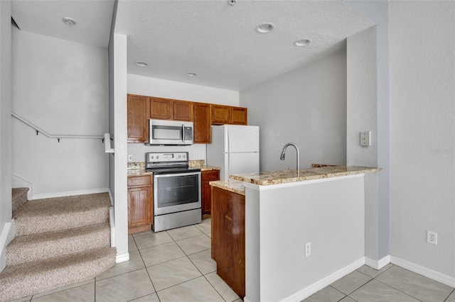 kitchen with light tile patterned flooring, appliances with stainless steel finishes, light stone counters, kitchen peninsula, and a textured ceiling