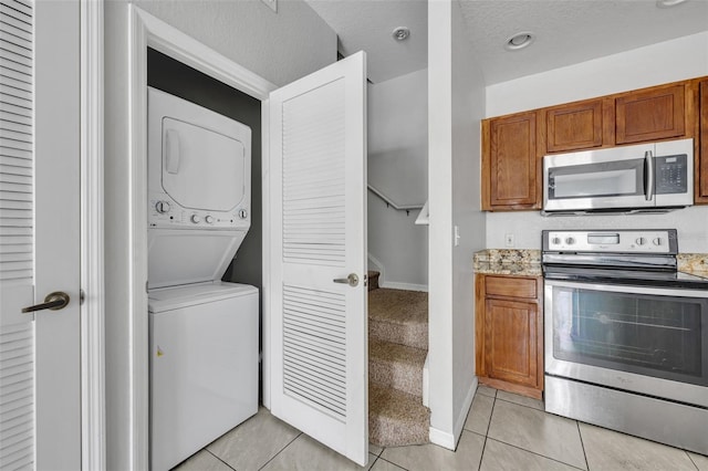 kitchen with stacked washer and dryer, light tile patterned flooring, appliances with stainless steel finishes, and a textured ceiling