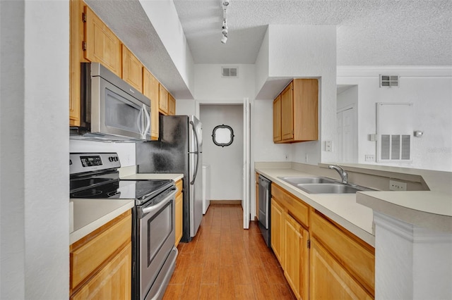 kitchen with appliances with stainless steel finishes, rail lighting, sink, a textured ceiling, and light hardwood / wood-style flooring