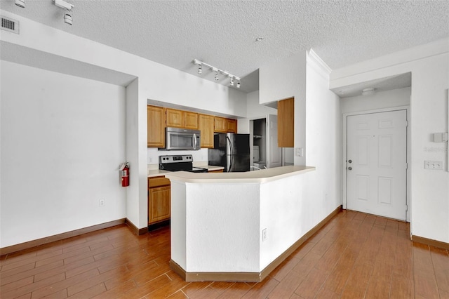 kitchen featuring appliances with stainless steel finishes, light hardwood / wood-style floors, kitchen peninsula, track lighting, and a textured ceiling