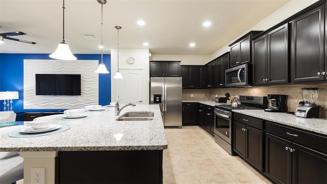 kitchen featuring sink, decorative light fixtures, stainless steel appliances, light stone countertops, and a kitchen island with sink