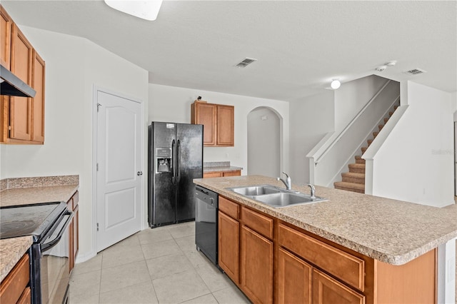 kitchen featuring sink, light tile patterned floors, black appliances, an island with sink, and a textured ceiling