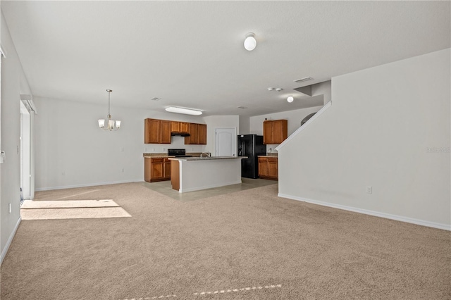 kitchen with an island with sink, a chandelier, hanging light fixtures, black fridge, and light carpet