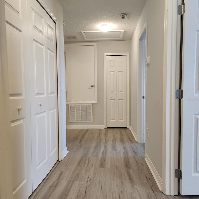 hall with baseboards, visible vents, attic access, a textured ceiling, and light wood-type flooring