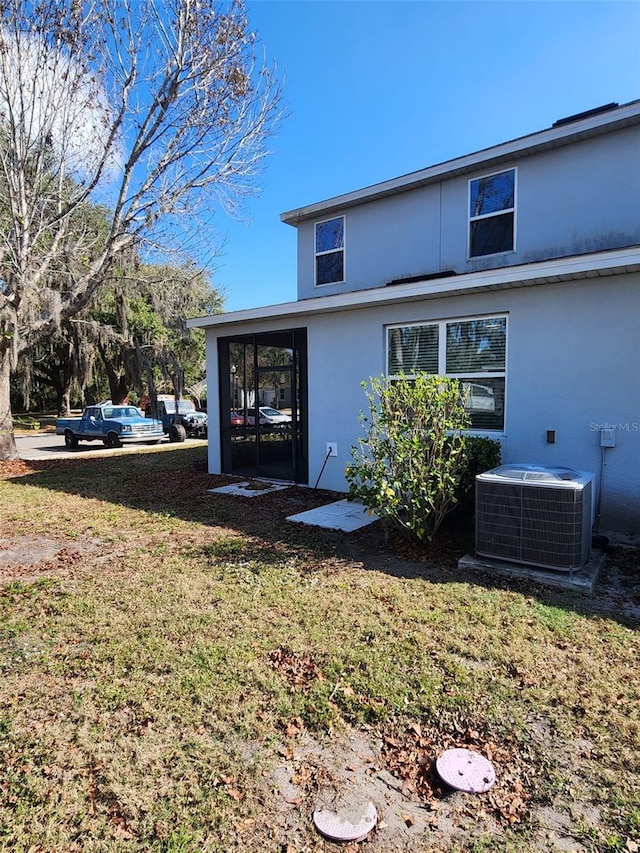 rear view of house with central air condition unit, a lawn, and stucco siding