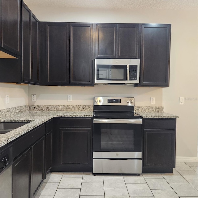 kitchen featuring stainless steel appliances, light stone countertops, and dark cabinets