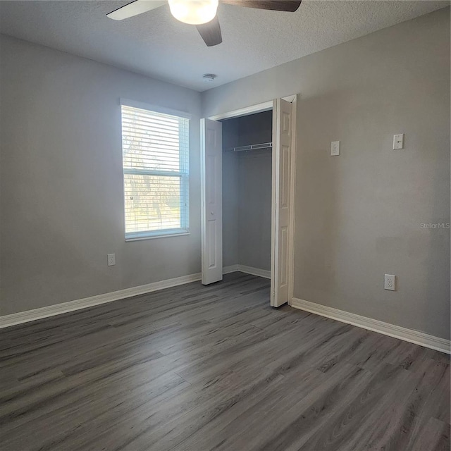 unfurnished bedroom featuring dark wood-type flooring, ceiling fan, baseboards, a closet, and a textured ceiling