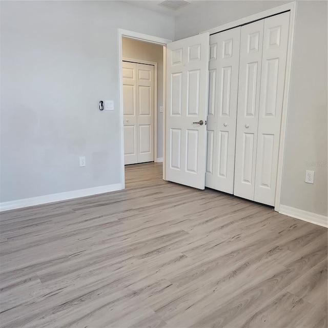 unfurnished bedroom featuring light wood-style flooring, baseboards, and a closet