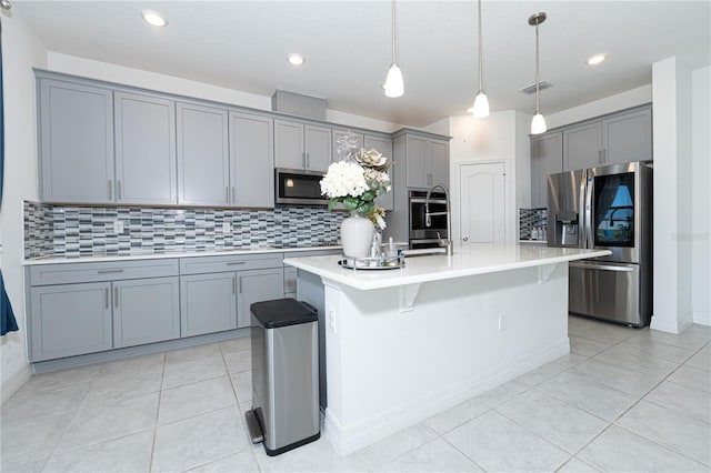 kitchen featuring gray cabinetry, light countertops, appliances with stainless steel finishes, an island with sink, and pendant lighting