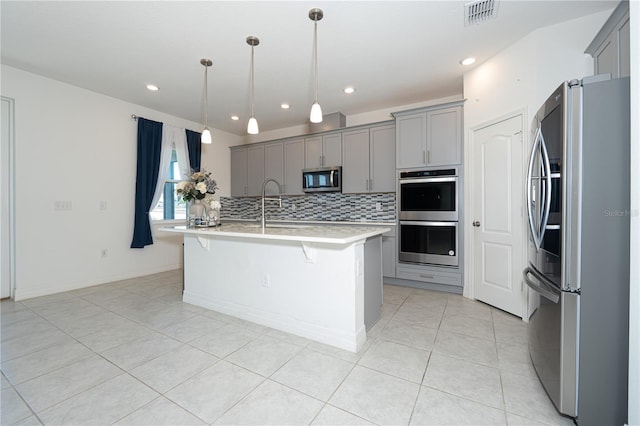 kitchen featuring a center island with sink, visible vents, appliances with stainless steel finishes, decorative light fixtures, and light countertops