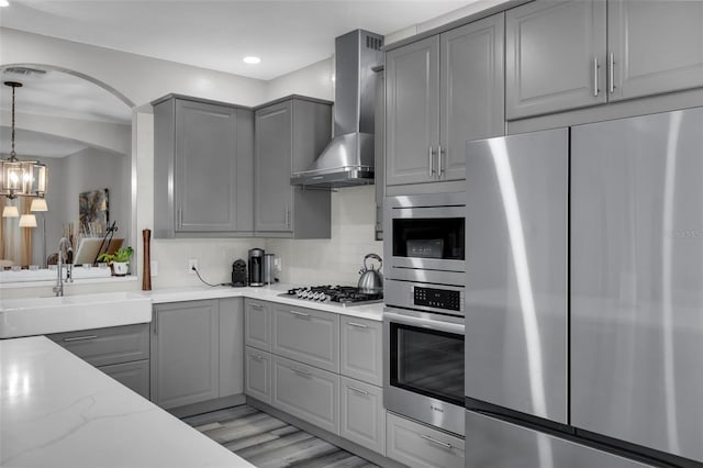 kitchen with appliances with stainless steel finishes, sink, gray cabinetry, backsplash, and wall chimney range hood