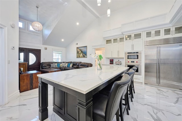 kitchen featuring light stone counters, stainless steel appliances, white cabinetry, marble finish floor, and a kitchen bar