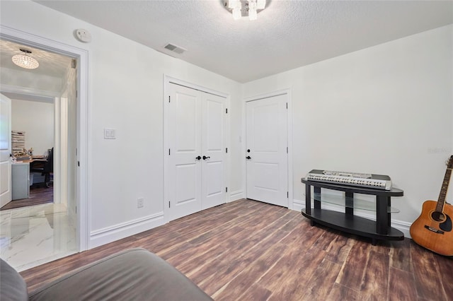 interior space with a textured ceiling, wood finished floors, visible vents, and baseboards