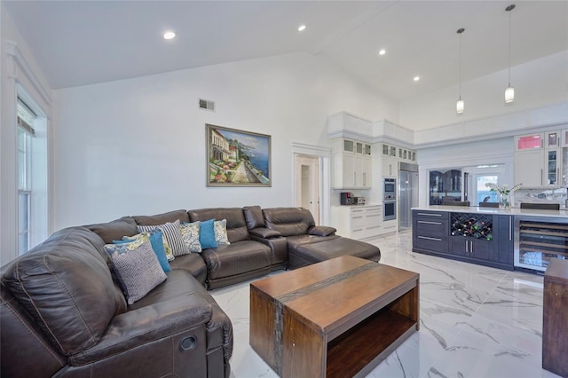 living room featuring high vaulted ceiling, beverage cooler, visible vents, marble finish floor, and a dry bar