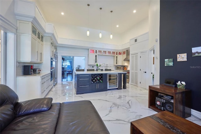 kitchen featuring beverage cooler, white cabinets, marble finish floor, light countertops, and wall chimney range hood