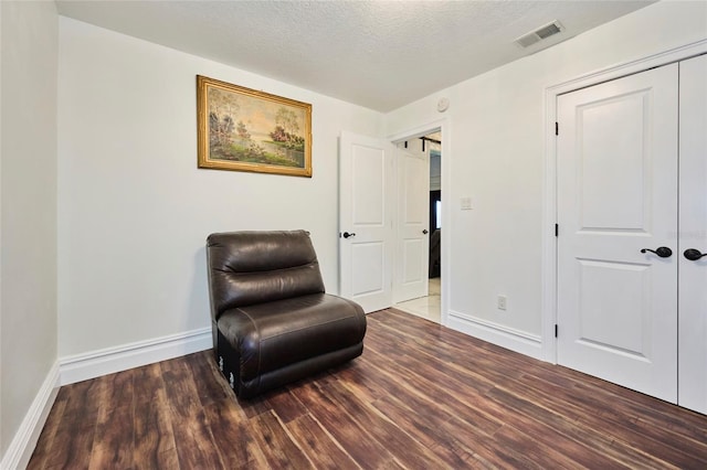 sitting room with visible vents, a textured ceiling, baseboards, and wood finished floors