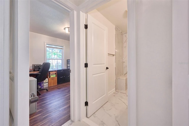 corridor with a textured ceiling and marble finish floor