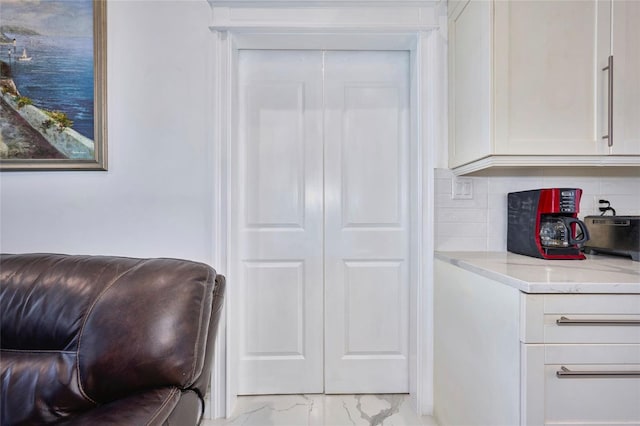 kitchen featuring light stone countertops, marble finish floor, white cabinetry, and decorative backsplash