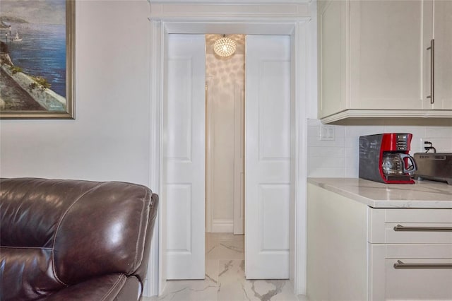 interior space with light stone counters, marble finish floor, white cabinetry, and backsplash