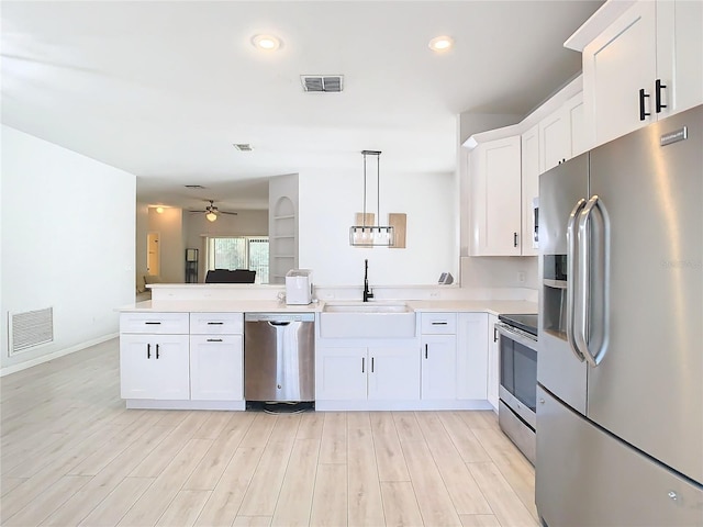 kitchen featuring sink, decorative light fixtures, appliances with stainless steel finishes, kitchen peninsula, and white cabinets