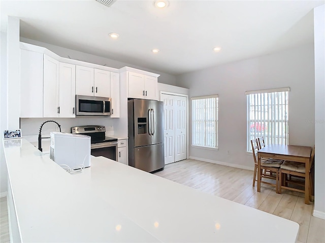 kitchen with appliances with stainless steel finishes, white cabinetry, sink, light hardwood / wood-style floors, and kitchen peninsula