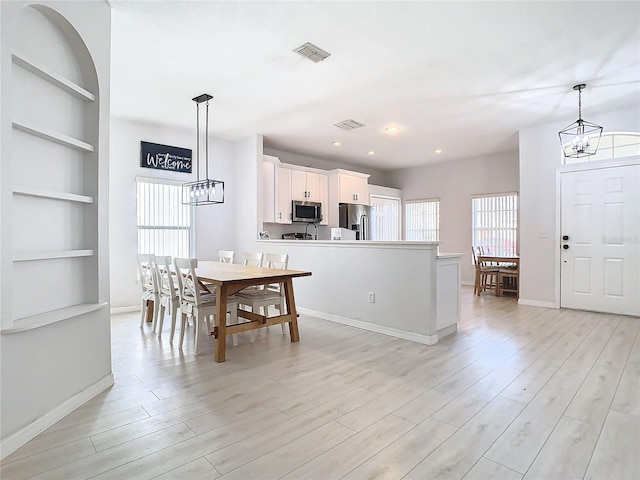 dining space with light hardwood / wood-style flooring, built in features, and a chandelier