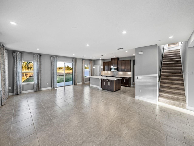 unfurnished living room featuring hanging light fixtures, dark brown cabinets, a center island, and sink