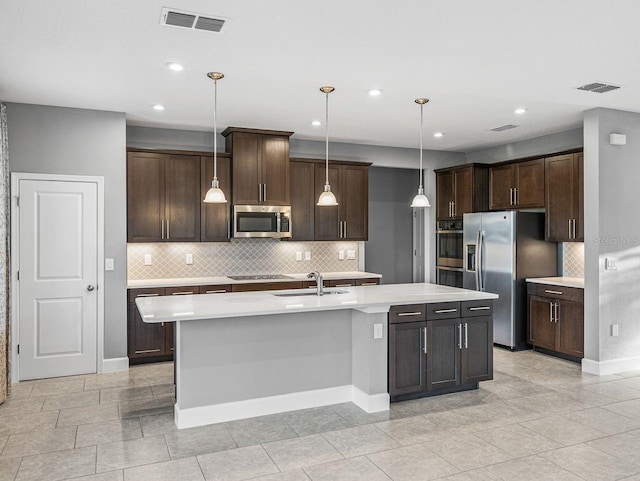 kitchen featuring an island with sink, appliances with stainless steel finishes, sink, and decorative light fixtures