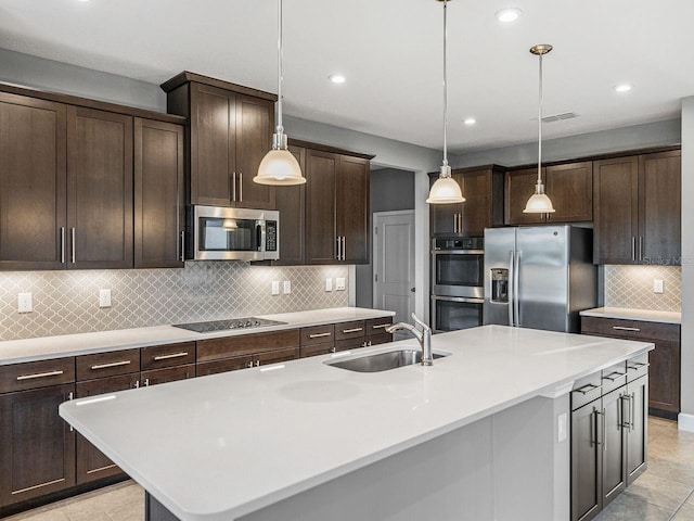 kitchen featuring sink, appliances with stainless steel finishes, a kitchen island with sink, hanging light fixtures, and dark brown cabinets