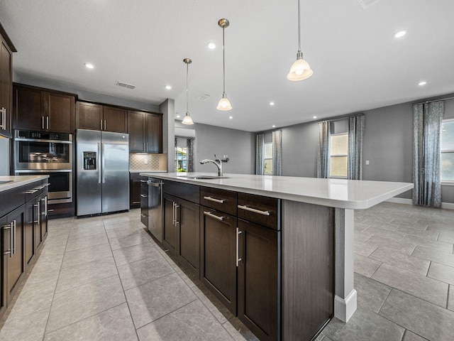 kitchen featuring dark brown cabinetry, sink, decorative light fixtures, appliances with stainless steel finishes, and a large island