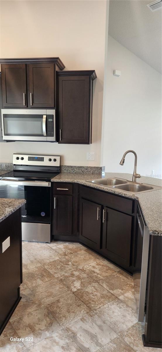 kitchen featuring sink, stone counters, stainless steel appliances, dark brown cabinetry, and vaulted ceiling