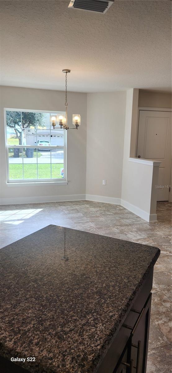 interior space featuring dark stone countertops, a textured ceiling, a chandelier, and decorative light fixtures